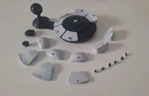 Joystick mit kugelförmigem Griff an einem runden Element mit austauschbaren grauen Tasten in unterschiedlichen Höhen. Die Tasten sind abgetrennt